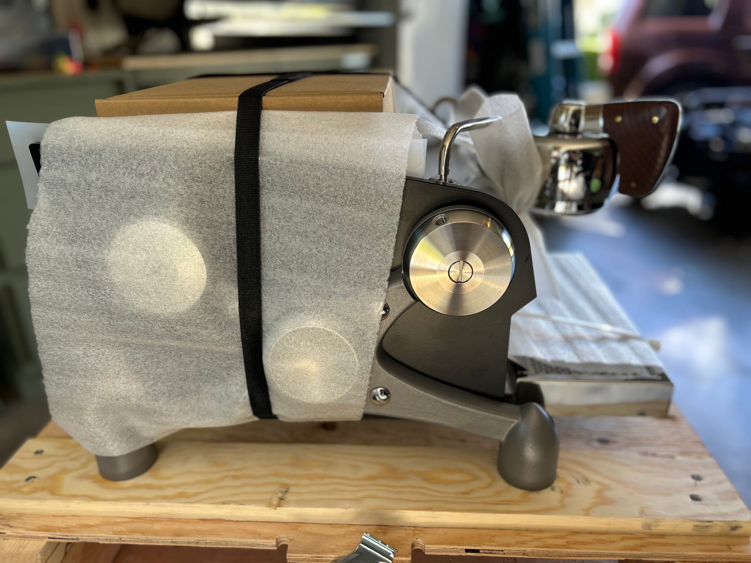 Slayer Espresso Single device with a wooden block on top, set against a blurred workshop background.
