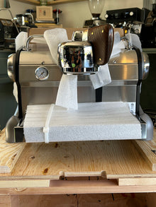 Slayer Espresso Single espresso machine on a wooden counter with a blurred coffee shop background