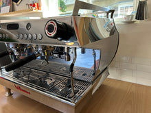 Professional espresso machine in a kitchen setting with a tiled wall and window in the background.