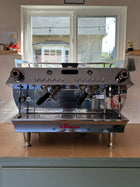 Commercial espresso machine on a wooden counter with a window in the background