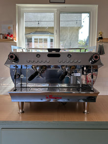 Commercial espresso machine on a wooden counter with a window in the background